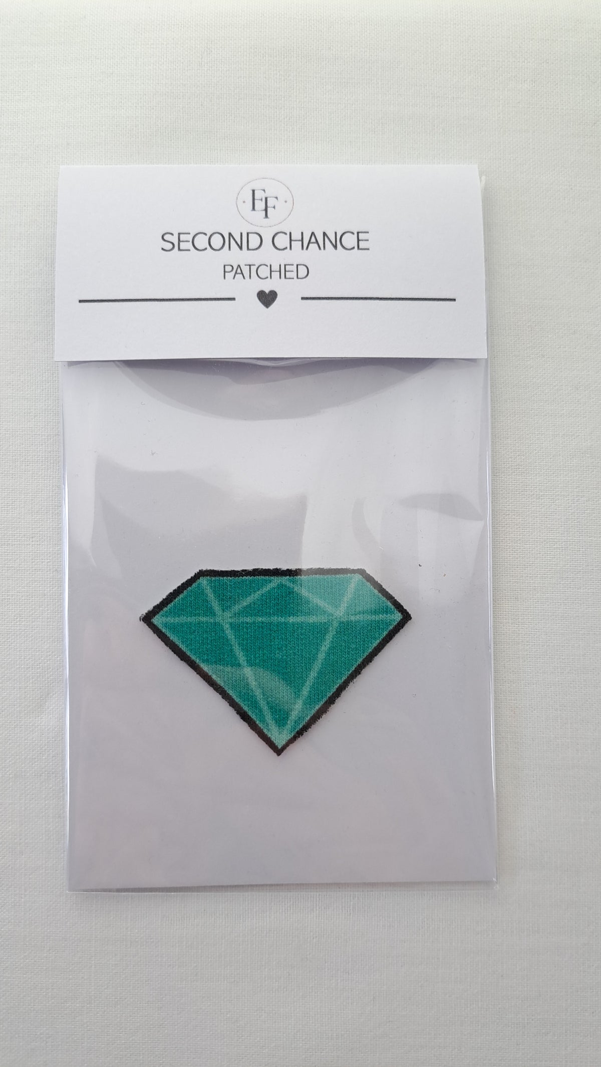 Nærbillede af Patched diamant-strygemærke i gennemsigtig Second Chance emballage
