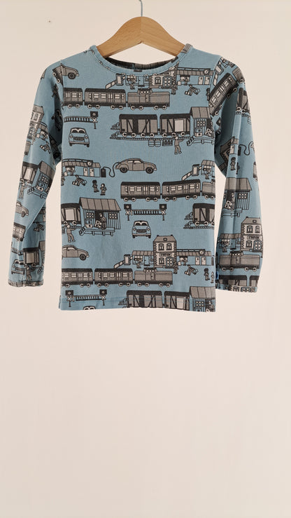 Lyseblå Småfolk langærmet børnebluse med print af tog, biler og bygninger set forfra