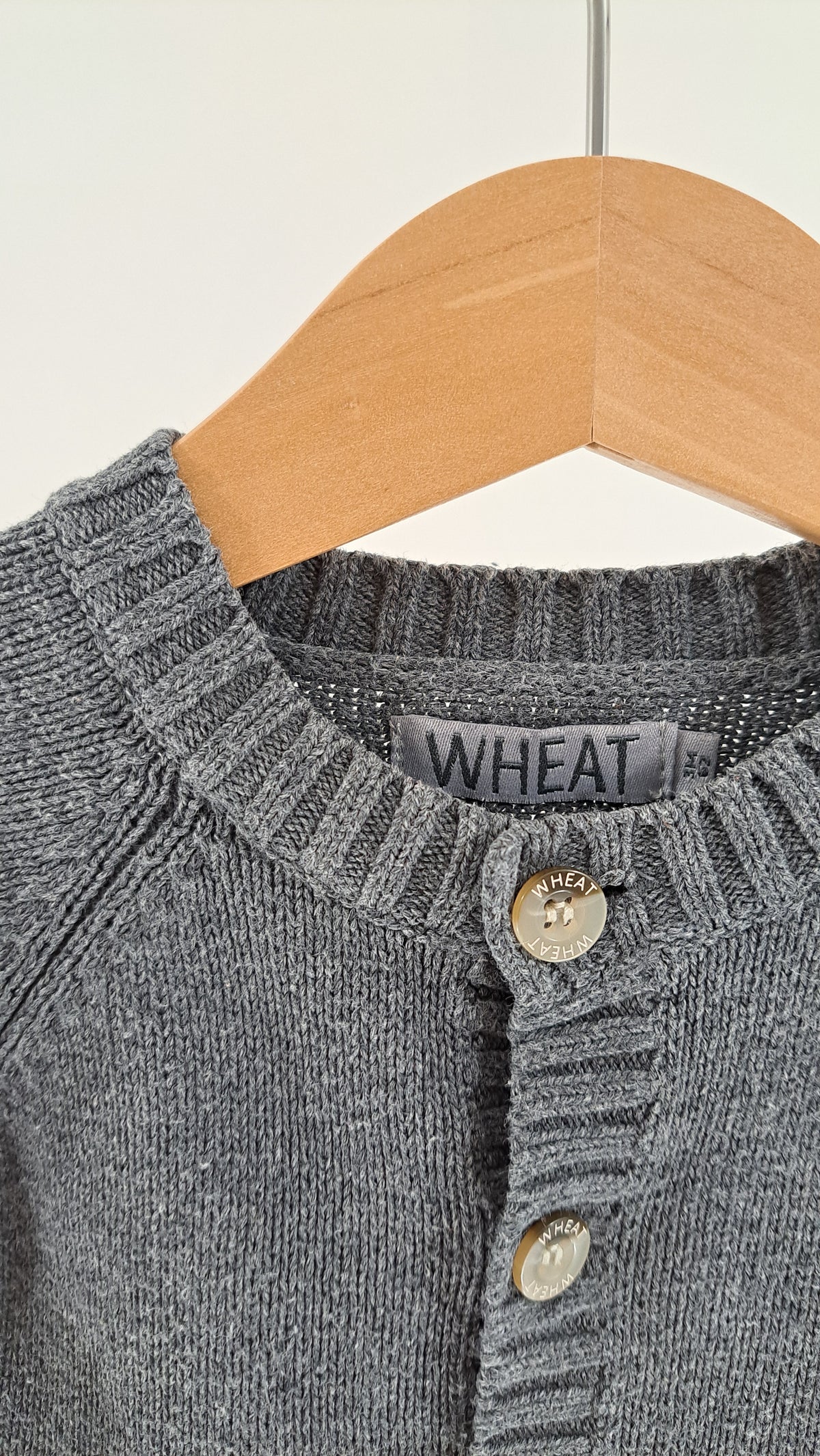 Nærbillede af halsudskæring, knaplukning og strikstruktur på Wheat cardigan