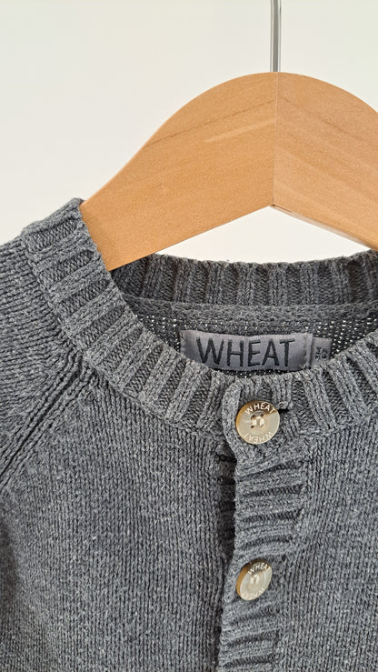 Nærbillede af halsudskæring, knaplukning og strikstruktur på Wheat cardigan