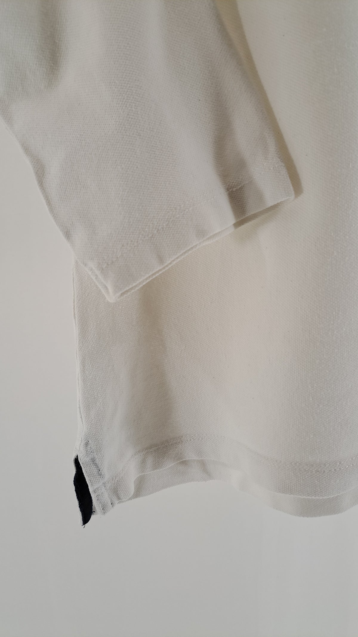 Nærbillede af sideslids med mørkeblåt bånd på hvid Tommy Hilfiger polo
