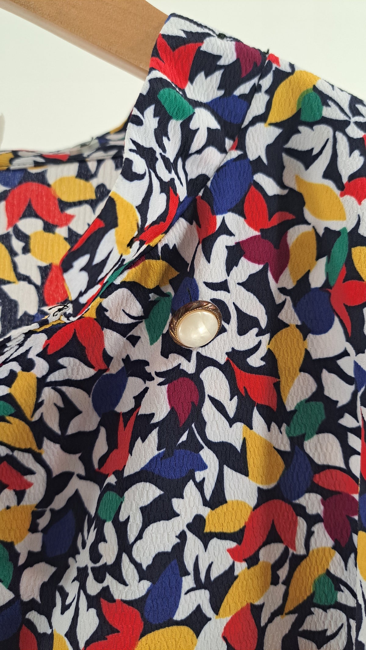 Nærbillede af knapdetalje på skulder af farverig vintage bluse