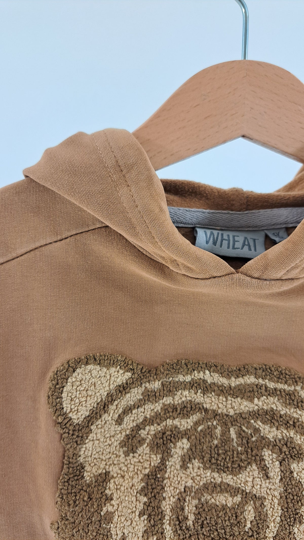 Nærbillede af bjørneapplikation og halsudskæring på brun Wheat hættetrøje